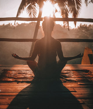Woman performing abundance meditation on deck at sunrise in Bali.