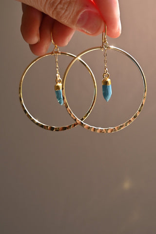 blue turquoise pendant hanging in center of gold hoop earrings